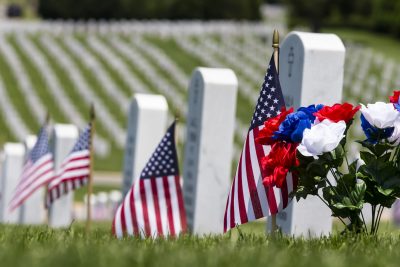 cemetary with military gravestones, small american flags, and red, white, and blur flowers
